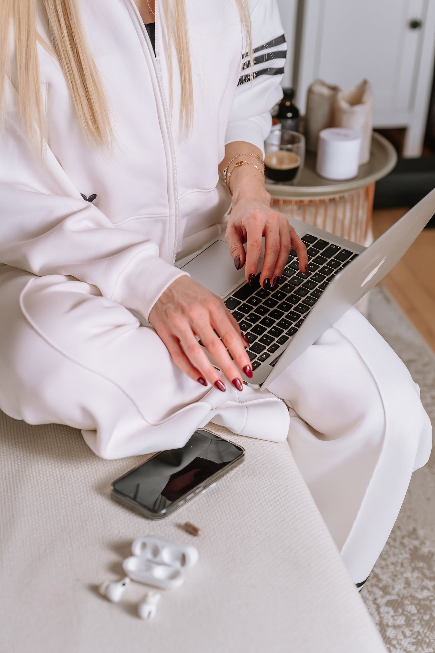 Eine Frau sitzt auf einer Couch mit einem Laptop, einem Handy und Airpods.