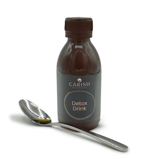 Der Detox Drink in einer dunkelbraunen Glasflasche und im Vordergrund ein Löffel mit ein paar Tropfen Detox Drink zur Ansicht.