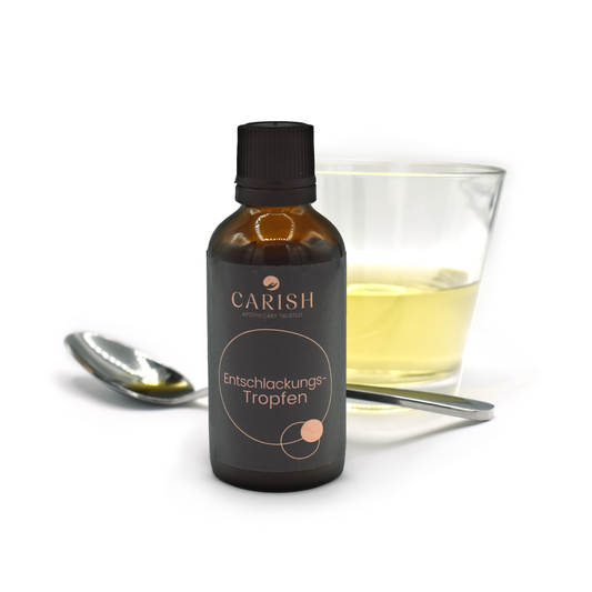 Im Vordergrund die dunkelbraune Flasche der Entschlackungstropfen und hinten ein Löffel und ein Glas mit den Tropfen befüllt zur Ansicht.