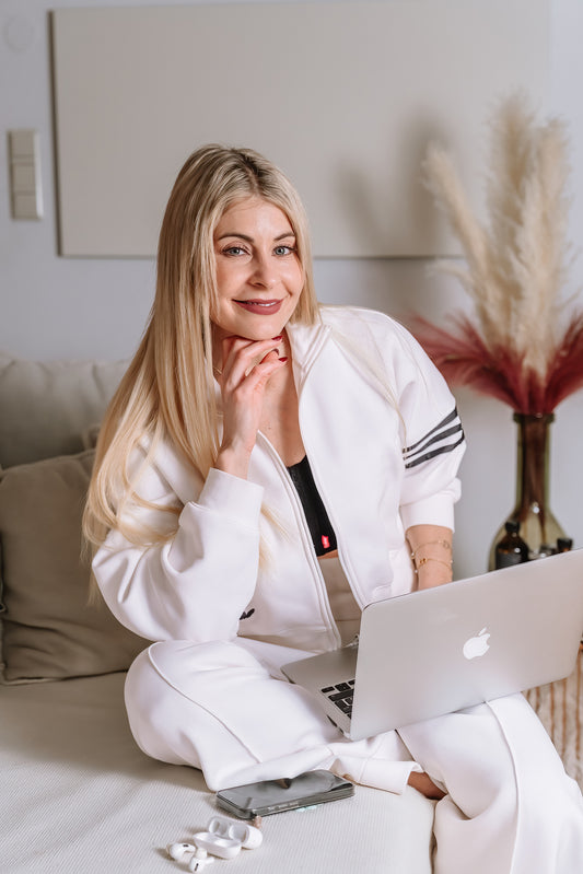 Nina Milenkovics sitzt in einem weißen Jogginganzug auf einer weißen Couch und hat einen Laptop auf ihrem Schoß.