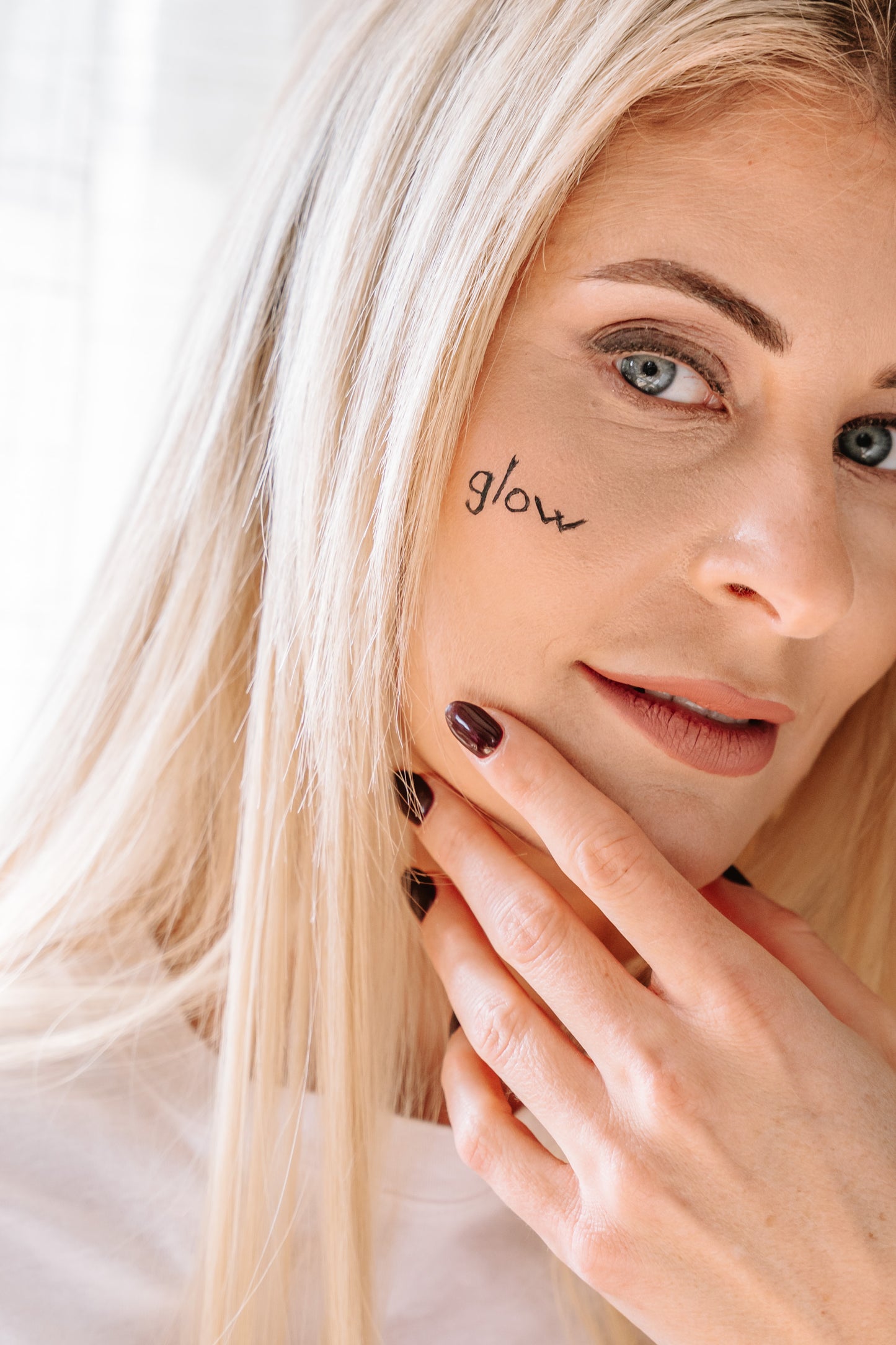Nina Milenkovics sieht direkt in die Kamera und hat auf ihrer Wange das Wort "glow" geschrieben.