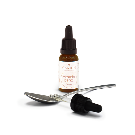 Die Vitamin D3 / K2 Tropfen in einer dunkelbraunen Glasflasche und im Vordergrund ein Löffel mit ein paar Tropfen und einer Ansicht der Pipette.
