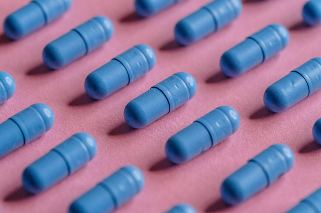 Ganz viele blaue Kapseln liegen auf einem rosa Papier aufgelegt in Reih und Glied. 