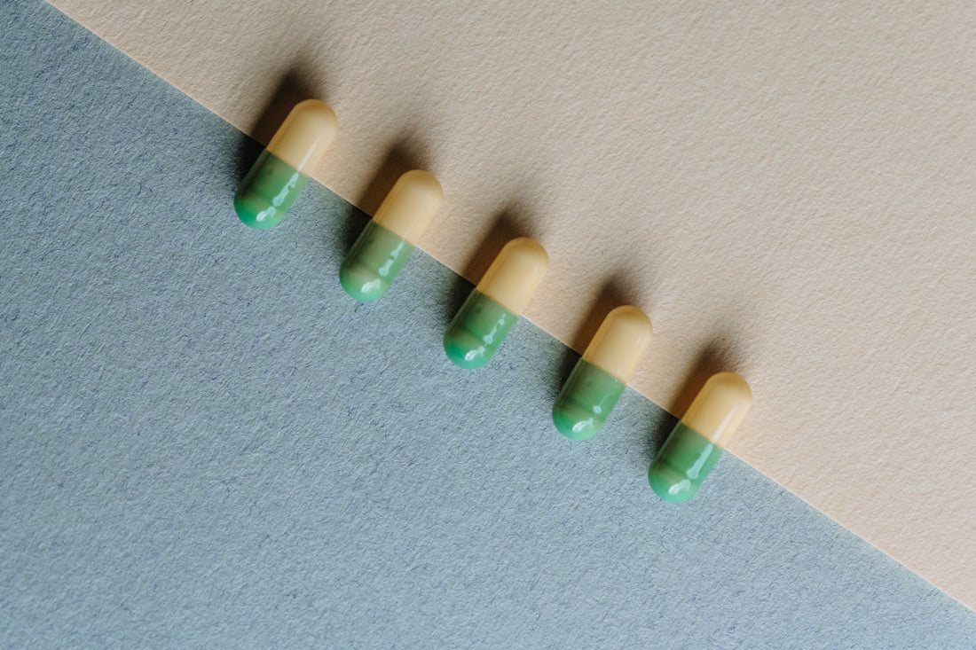 Grün - gelbe Kapseln liegen auf einer bunten Oberfläche und wurden von oben fotografiert.