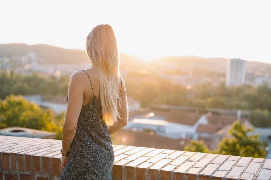 Nina Milenkovics steht vor einer Mauer mit dem Rücken zur Kamera und sieht sich den Sonnenuntergang über Graz an.