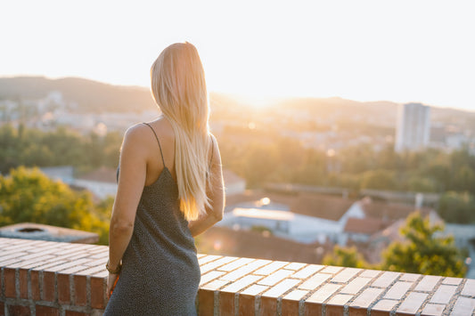 Nina Milenkovics steht vor einer Mauer mit dem Rücken zur Kamera und sieht sich den Sonnenuntergang über Graz an.
