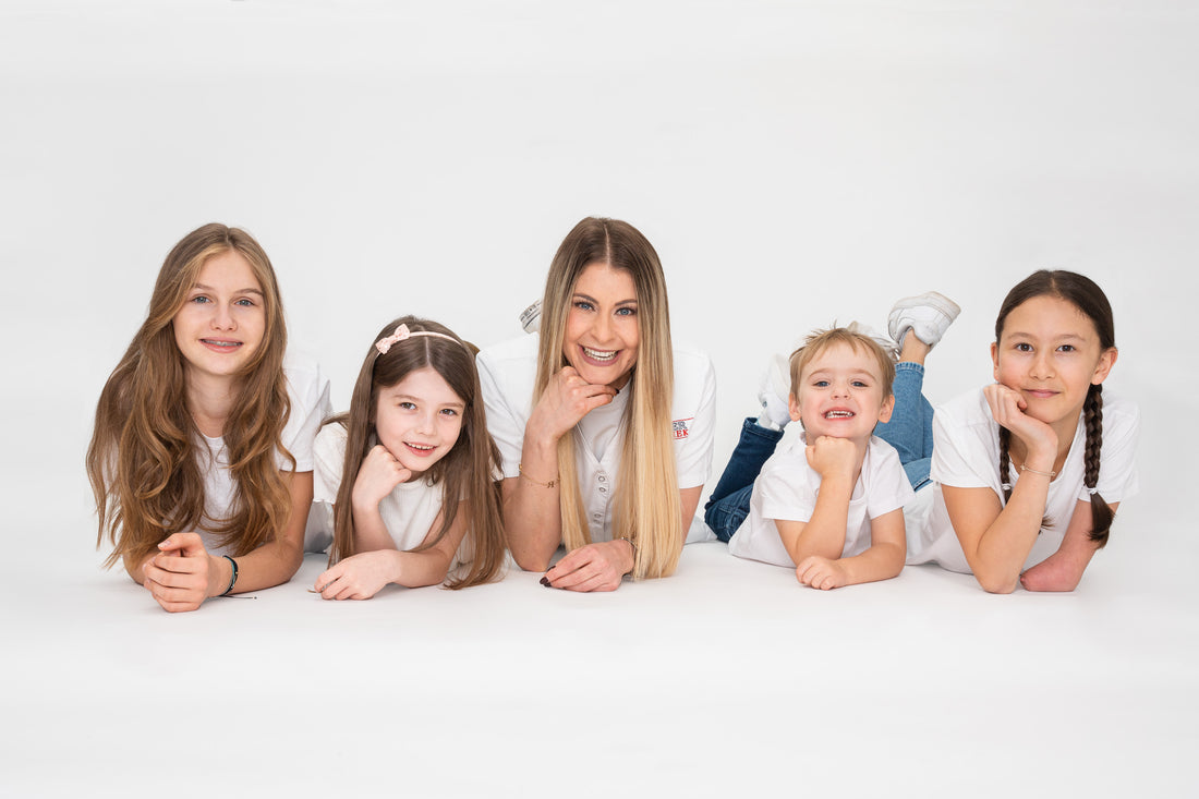 Nina Milenkovics liegt mit 4 Kindern am Boden und lacht in die Kamera.
