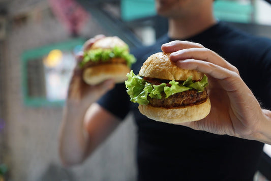 Man sieht einen Mann mit schwarzem T-Shirt der in jeder Hand einen Hamburger hält. 