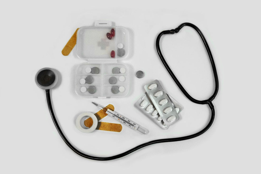Auf einem weißen Tisch liegen ein Stetoskop, Pflaster, Fieberthermometer, Tabletten.