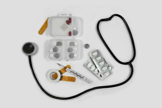 Auf einem weißen Tisch liegen ein Stetoskop, Pflaster, Fieberthermometer, Tabletten.