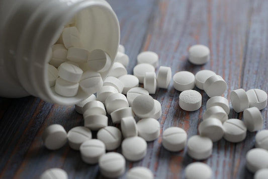 Auf einem Holztisch liegt eine geöfnette Tablettendose und viele weiße Tabletten sind überall verteilt.