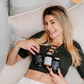 Die Apothekerin Nina Milenkovics liegt auf einer Couch, lacht in die Kamera und hat die 3 Produkte des Bauchwohl Pakets von Carish in ihren Händen. 