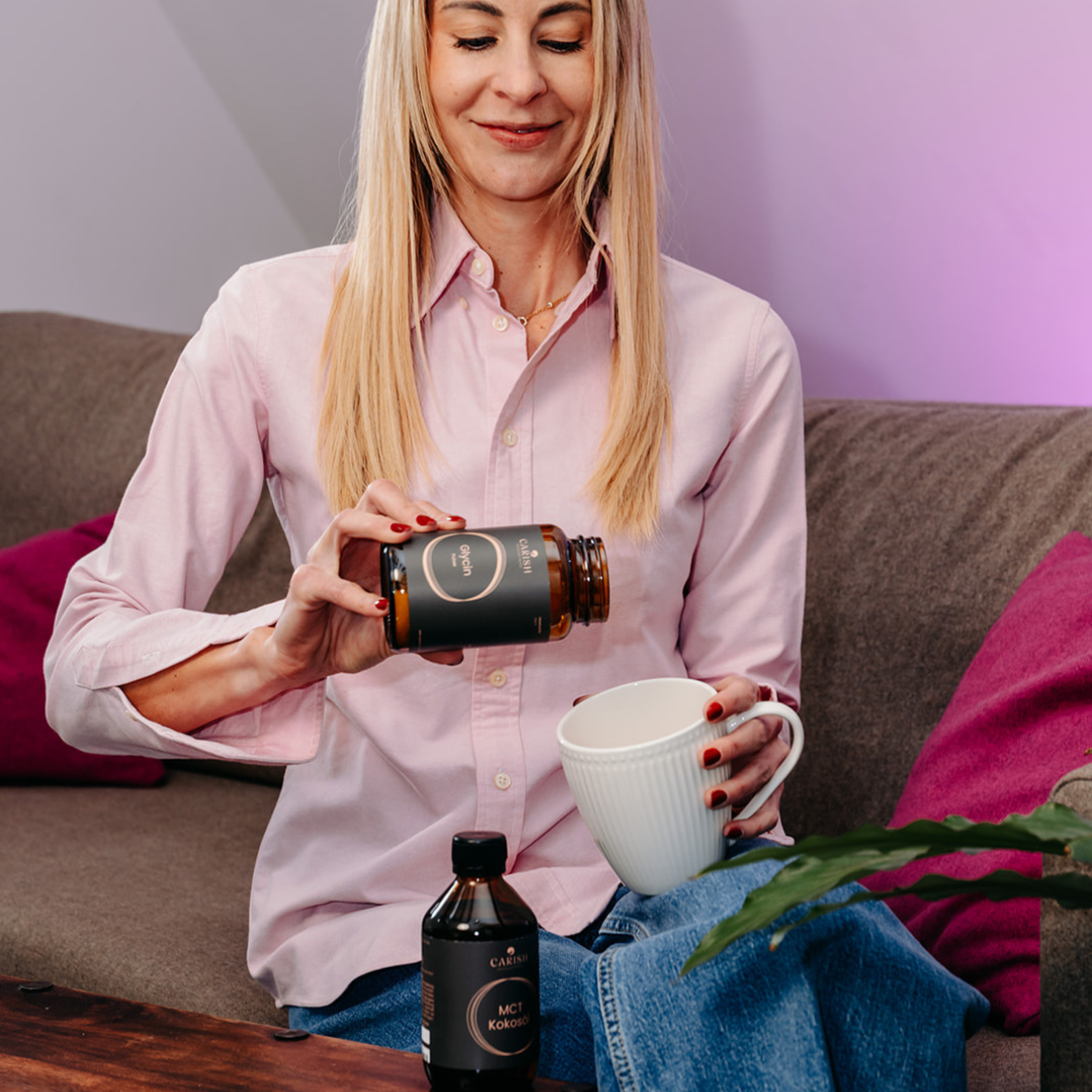 Nina Milenkovics sitzt auf einer Couch und schüttet sich etwas Glycin in ihren Bulletproof Kaffee. 