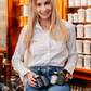 Nina Milenkovics sitzt auf einem Tisch, im Hintergrund alte Apothekengefäße und hält die 4 Produkte des Detoxpaket von Carish in ihren Händen. 