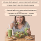 Eine Frau sitzt an einem Tisch und isst einen Salat. Sie hat in der linken Hand einen grünen Smoothie und Nüsse liegen überall verstreut. 