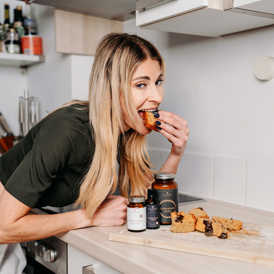 Die Apothekerin Nina Milenkovics steht in einer Küche und isst Kuchen. Vor ihr die 3 Produkte des Anti Heißhungerpaketes, das die Lust auf Süßes nimmt.