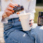 Eine Frau hält einen Kaffeebecher in der Hand und schüttet in wenig Glycin in den Becher. 