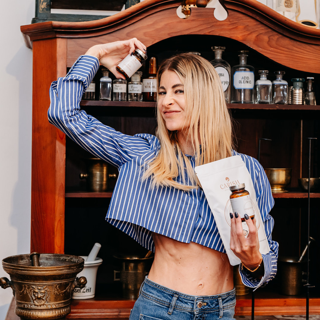 Nina Milenkovics steht vor einem Apothekerschrank und hat die 3 Produkte des Muskelpakets von Carish in ihren Händen. 
