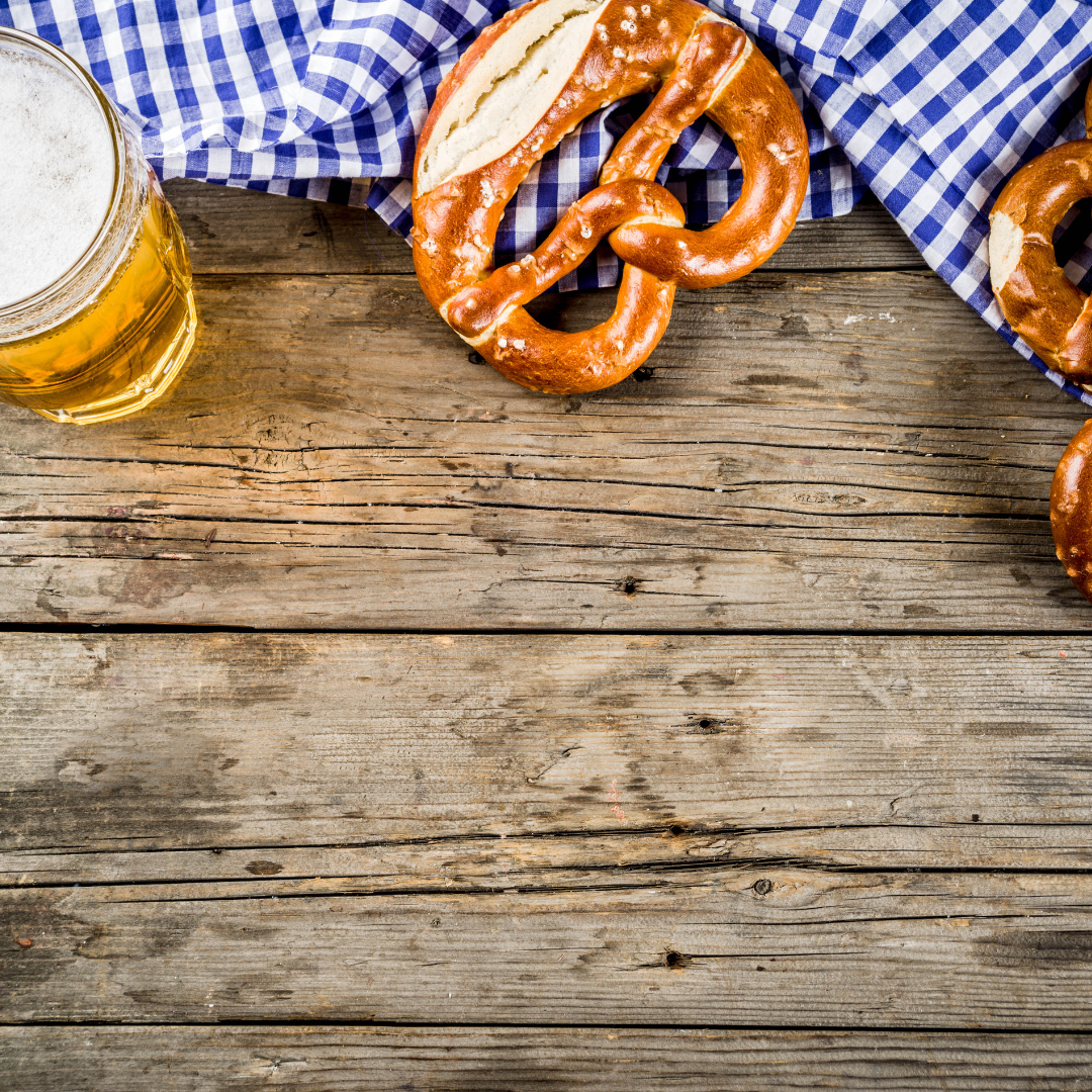 Auf einem alten Holztisch steht ein Krügerl Bier und 2 Brezen liegen daneben. 