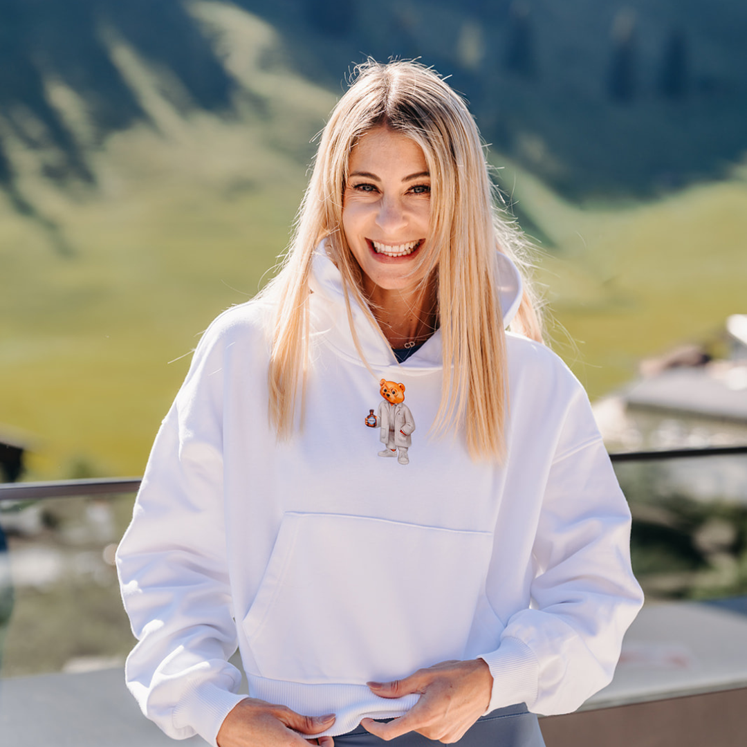 Nina Milenkovics trägt den Baron Filou Pullover in Zusammenarbeit mit Carish in weiß und lächelt in die Kamera. 