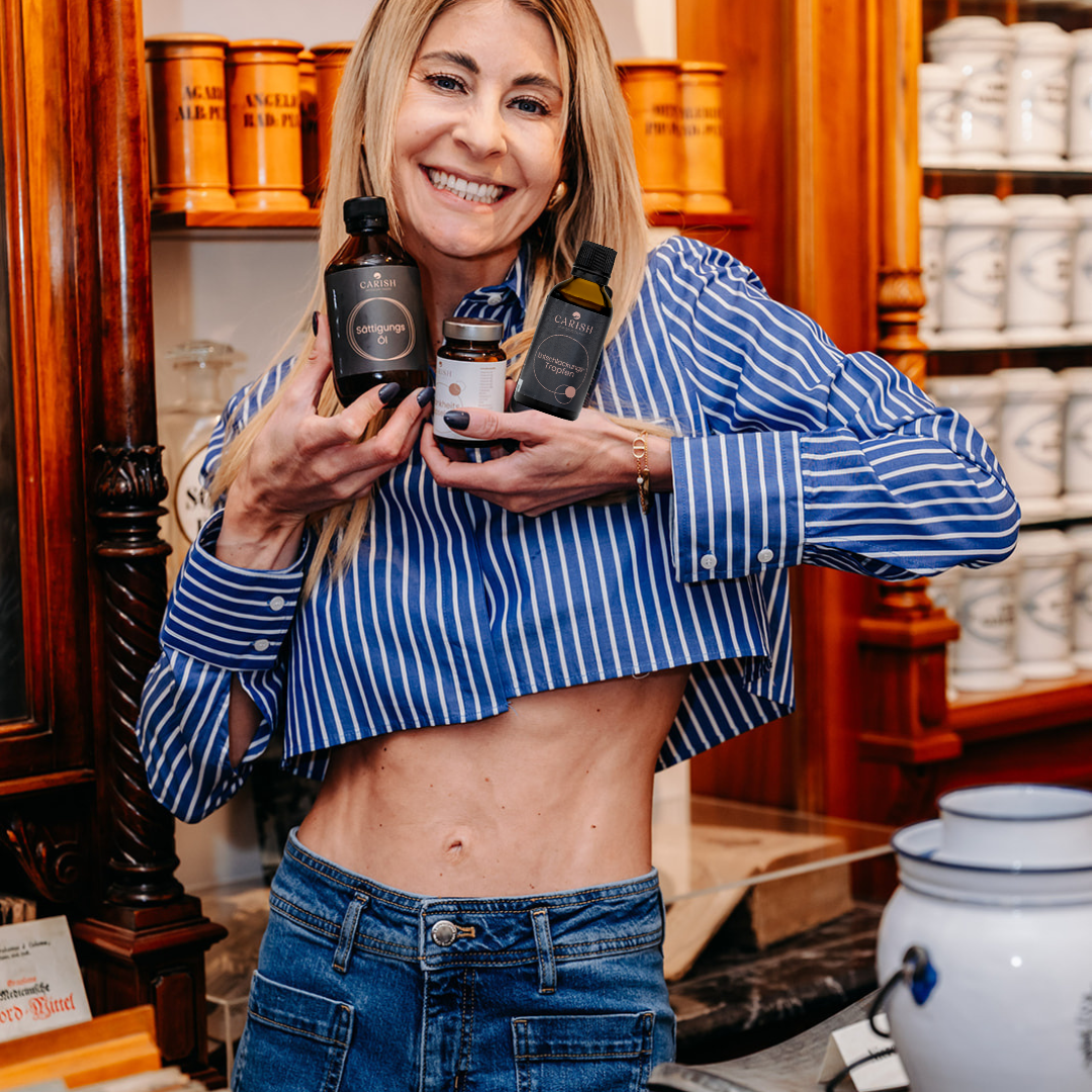 Die Apothekerin Nina Milenkovics steht vor einem Apothekerschrank und hält die 3 Produkte des Schlankheitspakets von Carish in die Kamera. 