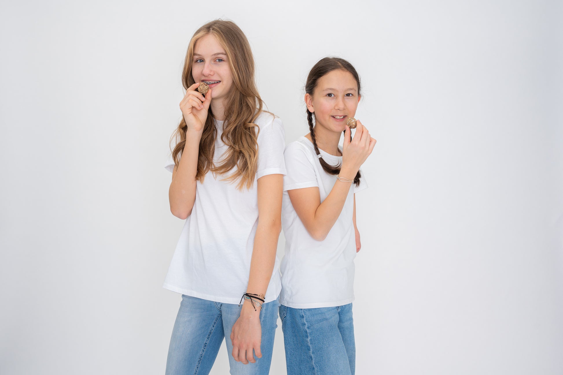 2 Mädchen mit weißem T-Shirt und blauer Jeans lächeln in die Kamera und haben ein Powerbällchen in der Hand.