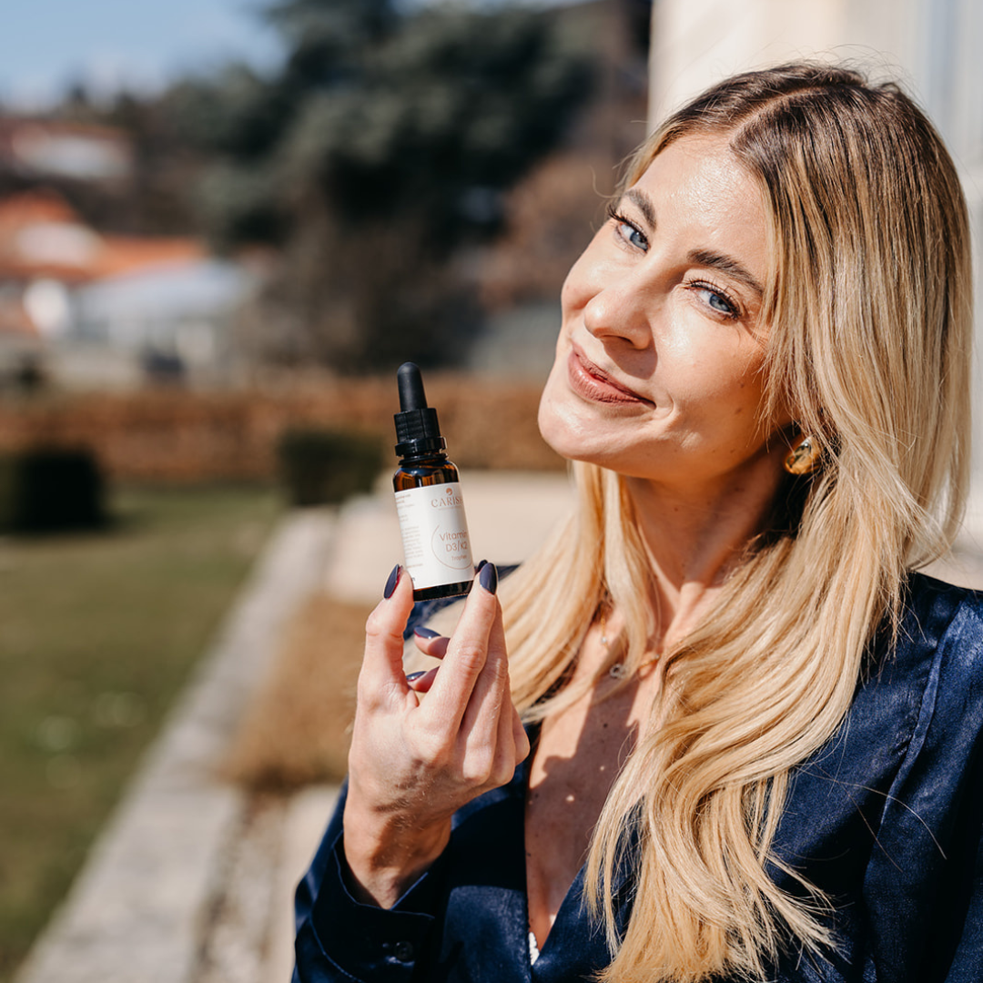 Nina Milenkovics steht in einem Park und hat die Vitamin D3 K2 Tropfen von Carish in ihren Händen. 